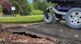Image description: The wheels of a powerchair
approaching a large bump in the sidewalk.