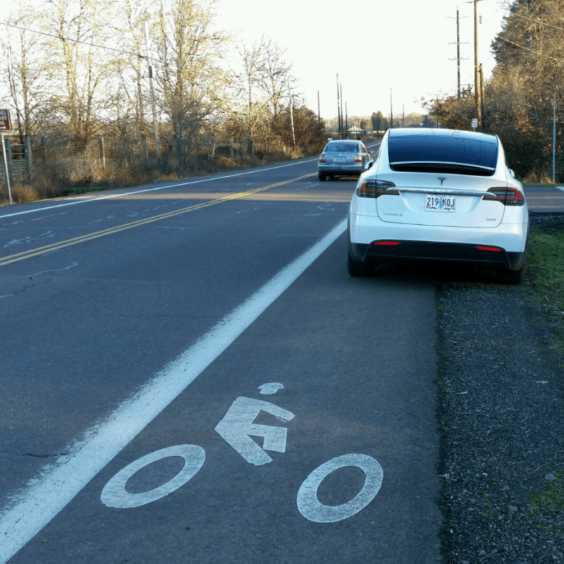 A Tesla driver parks in an unprotected bike lane. Image: Bike Lane Uprising